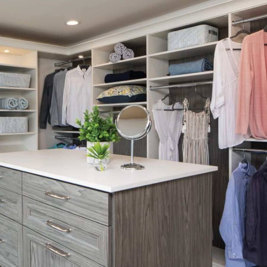 A closet with a custom shelving unit and island of drawers in the center of it